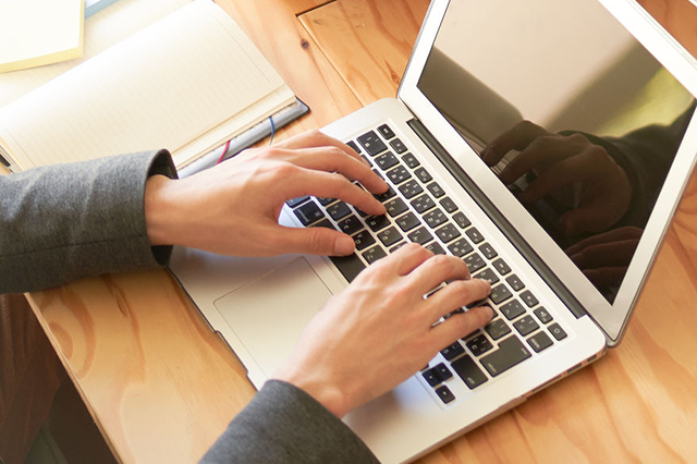 ノートパソコンで作業するスーツ姿の人物の手元、業務効率化や情報発信に関連するイメージ