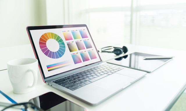 カラーパレットを表示したノートパソコンと周辺機器が置かれた明るいオフィスデスク、Webアクセシビリティ対応を意識したデザイン作業のイメージ
