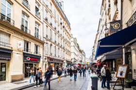 パリの商店街で多くの歩行者が行き交う石畳の通りと両側に並ぶ店舗やカフェ